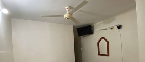 Ein Zimmer mit zwei Betten, einem Deckenventilator, einem an der Wand befestigten Fernseher und einem Sessel.