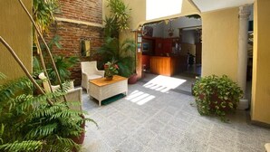 Une cour intérieure avec un mur en briques, des plantes en pot, des meubles en osier et un espace d’accueil.