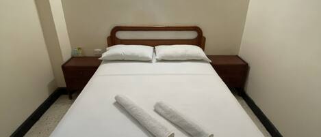 Una cama individual con estructura de madera, ropa de cama blanca y dos toallas enrolladas.
