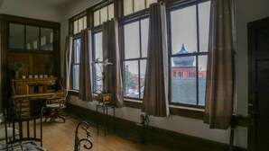 Une pièce dotée de grandes fenêtres, d’un bureau en bois, d’une chaise et d’une lampe.