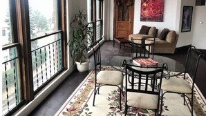 Un salon chaleureux avec un canapé, une table basse et une table à manger avec des chaises. Une grande fenêtre offre une vue sur l’extérieur, et on y trouve également une plante en pot et un tableau accroché au mur.