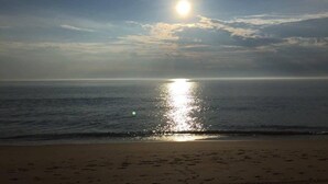 A beach with a clear sky, sun reflecting on the water, and a sandy shore. - Waterfront Gorgeous Beach Home-Sunsets & Spa Bath (Duck)