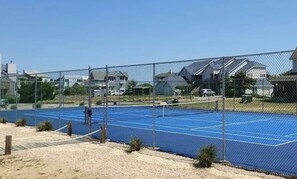 A tennis court with a chain-link fence, surrounded by houses and a clear sky. - Waterfront Gorgeous Beach Home-Sunsets & Spa Bath (Duck)