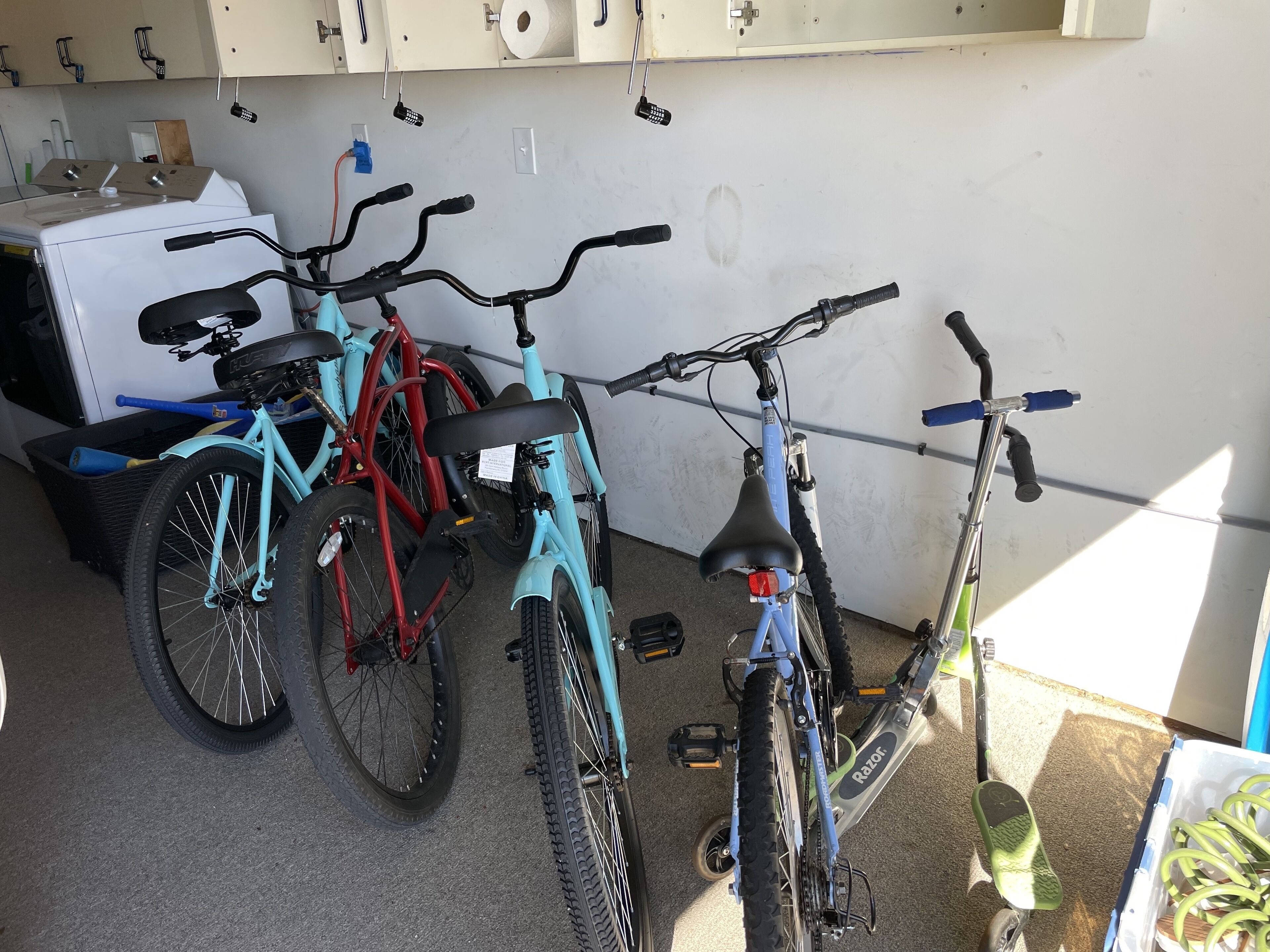 A garage with three bicycles, a washing machine, and a trash bin.