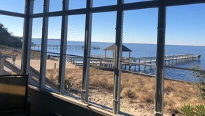 A view through large windows of a beach area with a wooden pier and a small gazebo. - Waterfront Gorgeous Beach Home-Sunsets & Spa Bath (Duck)