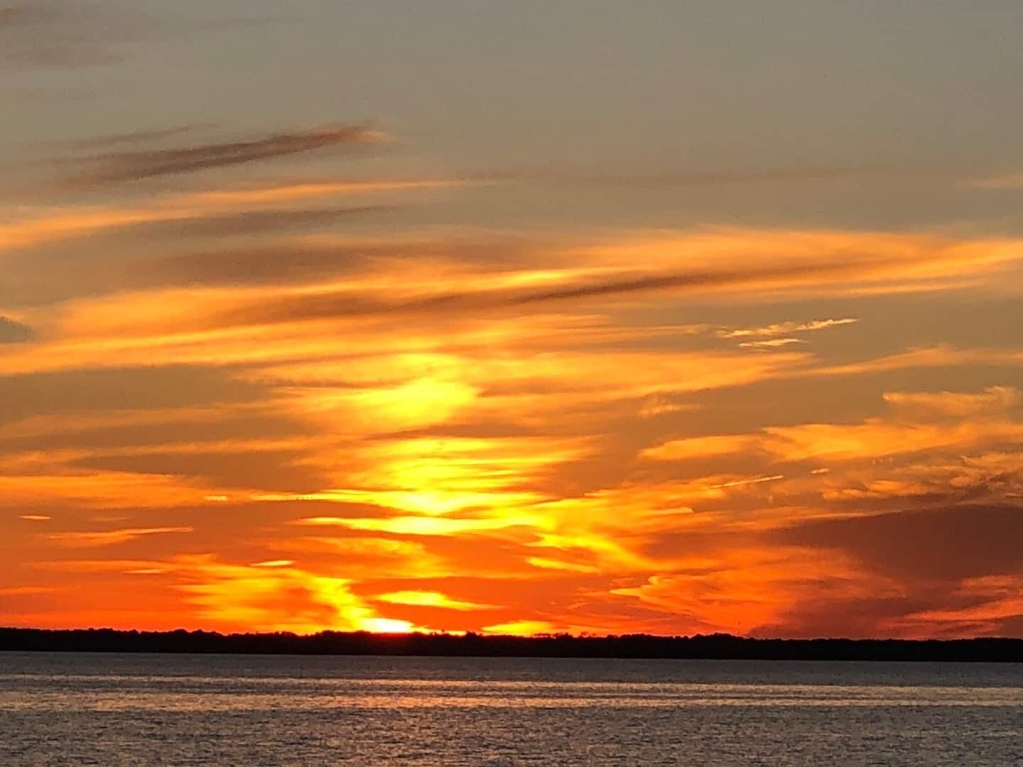 Un coucher de soleil sur une étendue d’eau, avec la silhouette d’une côte lointaine.