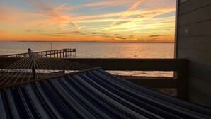 A hammock on a wooden deck overlooking a sunset over the water. - Waterfront Gorgeous Beach Home-Sunsets & Spa Bath (Duck)