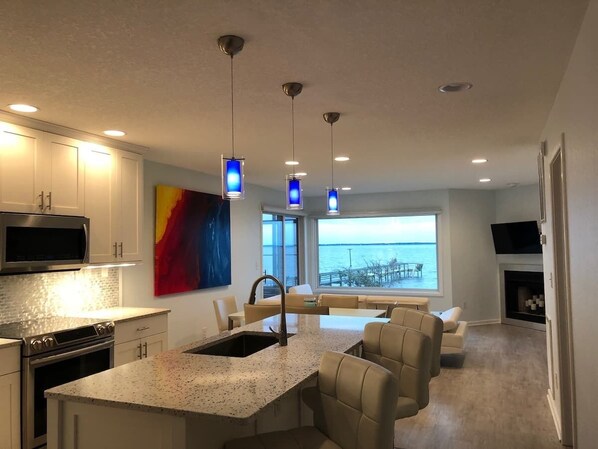 A modern kitchen with a large island, stainless steel appliances, and pendant lighting. - Waterfront Gorgeous Beach Home-Sunsets & Spa Bath (Duck)