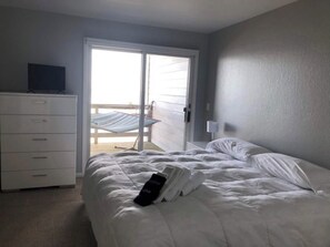 A hotel room with a bed, a dresser, a television, and a balcony with a chair. - Waterfront Gorgeous Beach Home-Sunsets & Spa Bath (Duck)