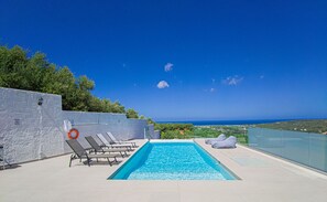 A swimming pool with lounge chairs, a lifebuoy, and a view of the sea. - Modern villa with infinity pool close to the sea (Πολεμάρχι)