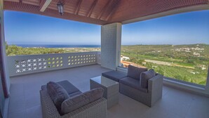 Ein Balkon mit Korbmöbeln und freiem Blick auf das Meer und die Landschaft.