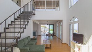Ein geräumiger Wohnbereich mit Treppe, einem grünen Sofa, einem Esstisch und einem Fernseher auf einem Schrank.
