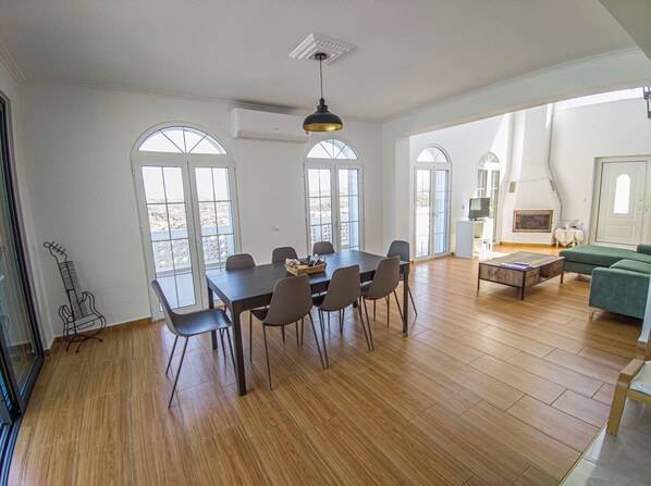 A spacious room with a wooden floor, a dining table with chairs, a sofa, and a fireplace. - Modern villa with infinity pool close to the sea (Πολεμάρχι)