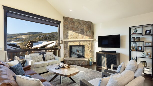 A spacious living room with a stone fireplace, a flat-screen TV, and a large window offering a scenic view. - Private Hot Tub/Brand New Luxury Townhome/Short Drive to Slopes! (Keystone)