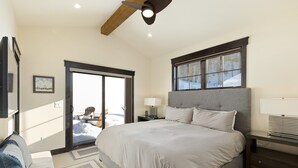 A bedroom with a large bed, a ceiling fan, a window with a view of snow, a nightstand with a lamp, and a door leading outside. - Private Hot Tub/Brand New Luxury Townhome/Short Drive to Slopes! (Keystone)