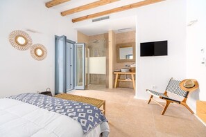 Une chambre à coucher avec un lit, une chaise, un téléviseur et une salle de bain visible à travers une porte ouverte.