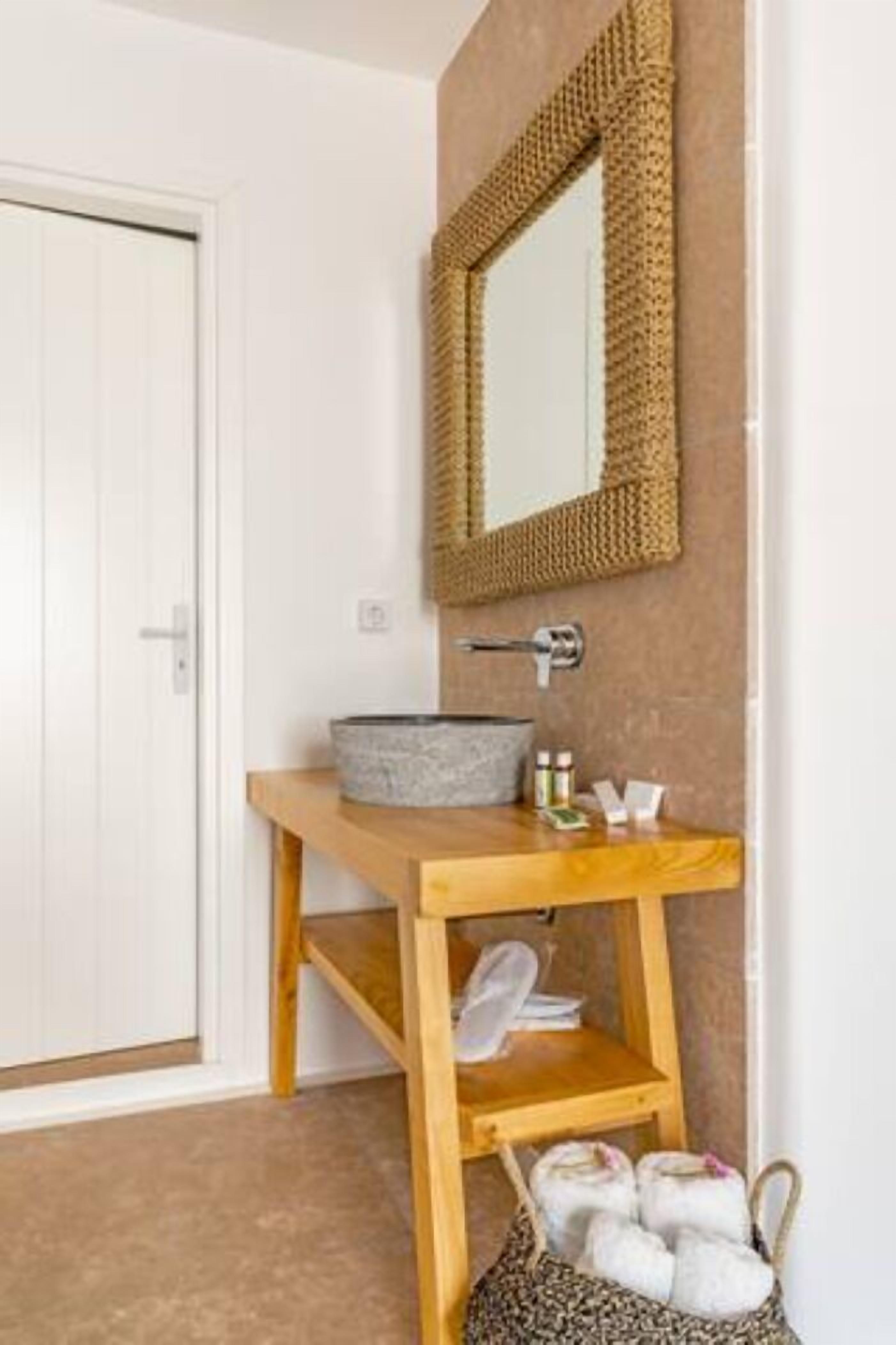 A bathroom with a wooden vanity, a stone sink, a woven mirror frame, and a shelf with towels and toiletries.