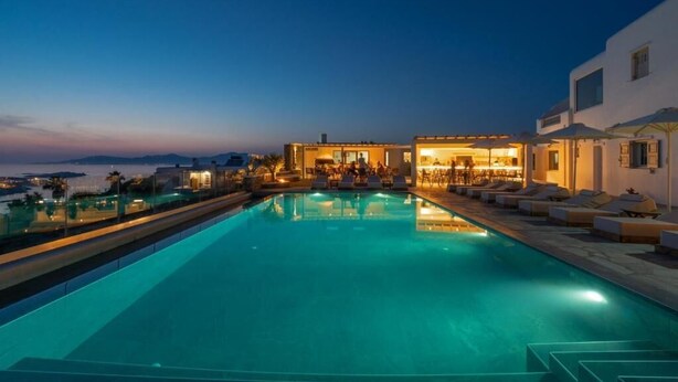 Zona de piscina con bar y sillones, con vistas a un cuerpo de agua y colinas.