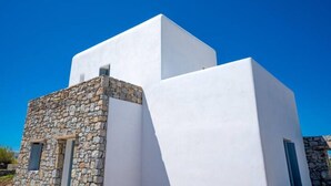 Un edificio moderno con base de piedra y secciones superiores blancas, bajo un cielo azul despejado.