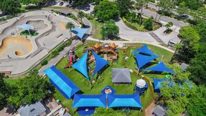 Eine Vogelperspektive auf einen Park mit einem Spielplatz, einer großen, blauen, tentartigen Konstruktion und einer kurvenreichen Straße.