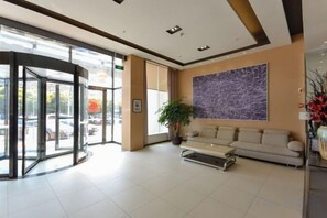 A hotel lobby with a revolving door, a sofa, a potted plant, and a large abstract painting on the wall. - Jinjiang Inn (Xianju Huancheng North Road) (Xianju)