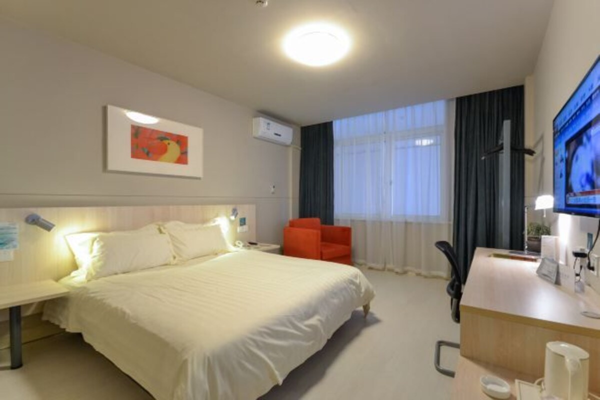 Habitación de hotel con cama, escritorio, silla, televisor y ventana con cortinas.