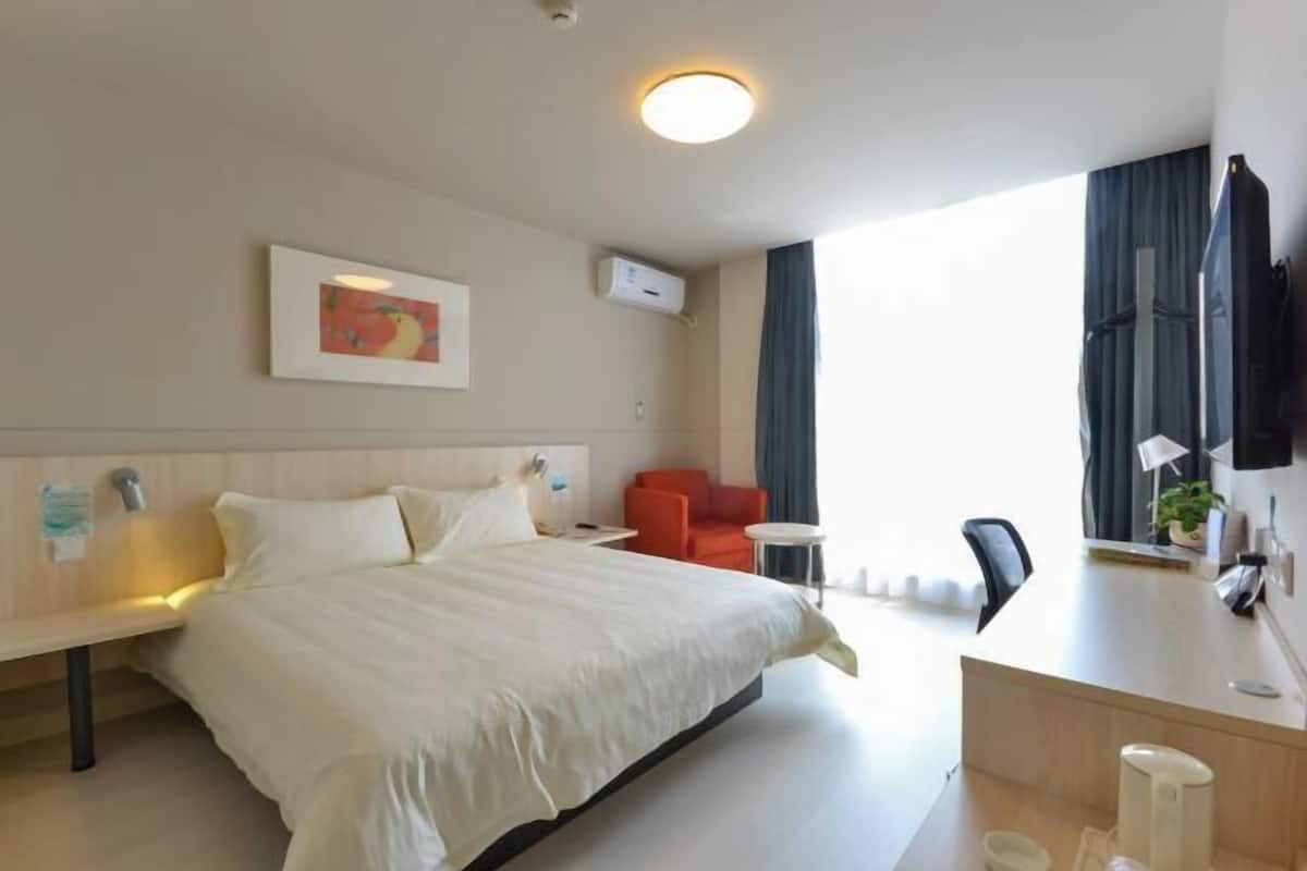 A hotel room with a bed, a desk, a chair, a TV, and a window with curtains.