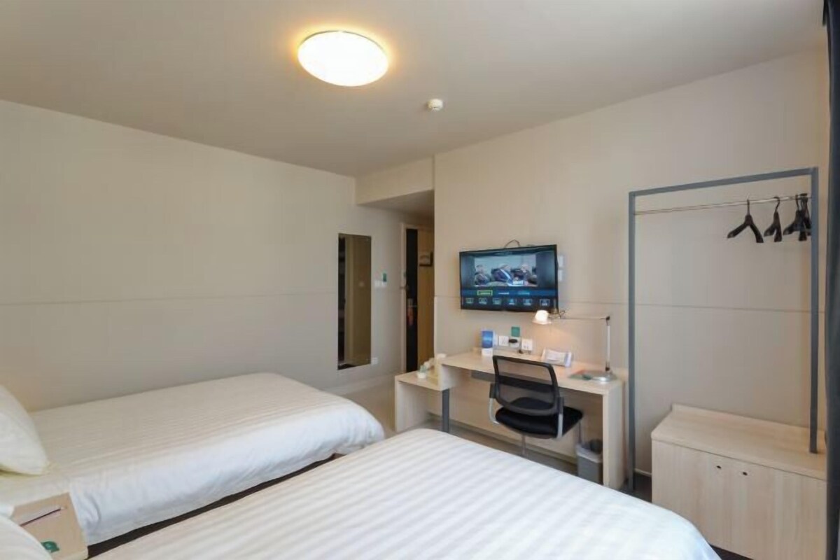 A hotel room with two beds, a desk, a TV, and a wardrobe.