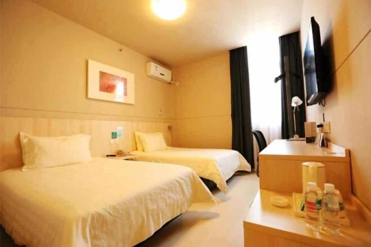 A hotel room with two beds, a TV, a desk with a lamp, and a framed picture on the wall.