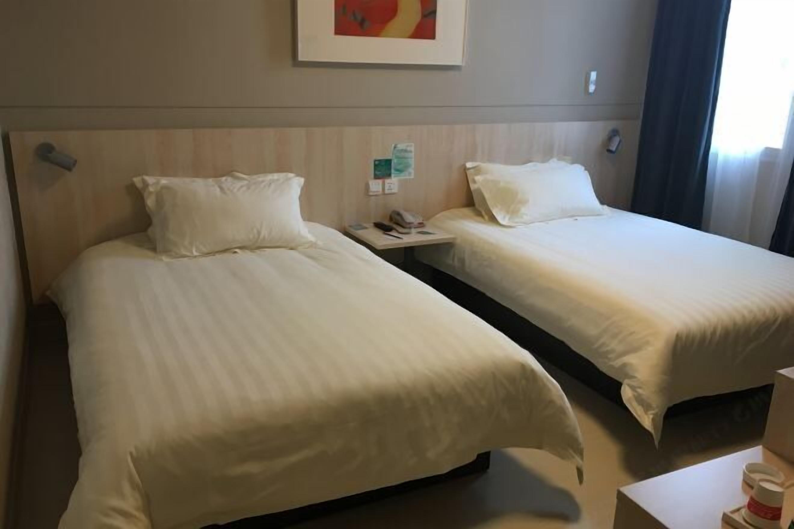 Habitación de hotel con dos camas, una mesita de noche, un cuadro en la pared y una ventana con cortinas.