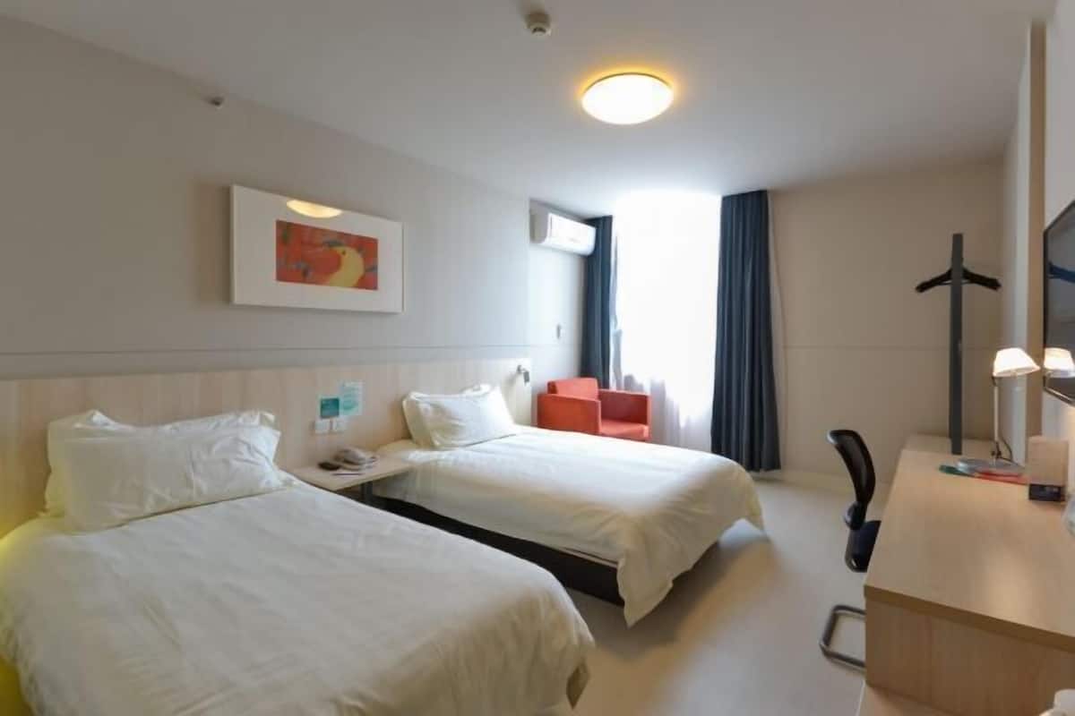 A hotel room with two beds, a desk, a chair, a TV, and a window with curtains.