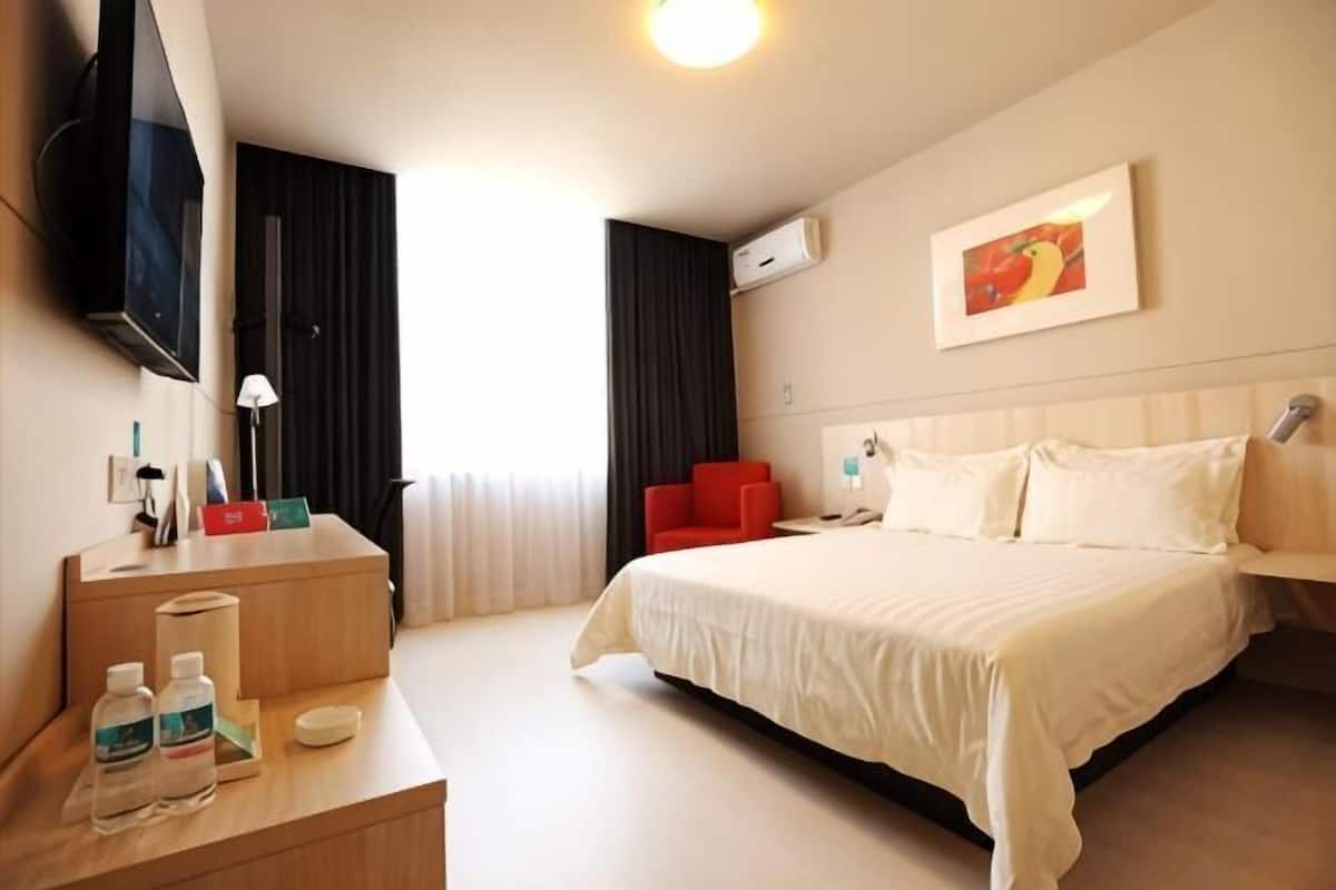 A hotel room with a bed, a desk with toiletries, a TV, and a painting on the wall.