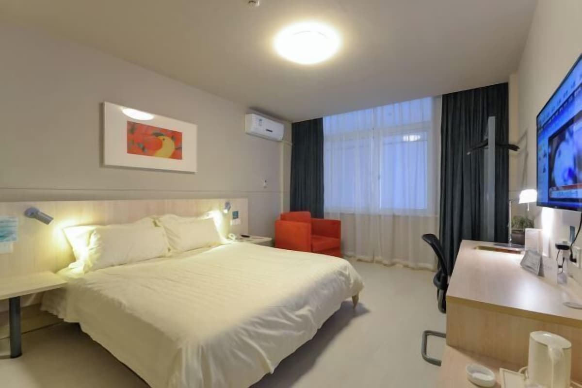 A hotel room with a bed, a desk, a chair, a TV, and a window with curtains.