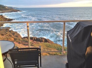 A balcony with a view of the ocean, a grill, and a chair.