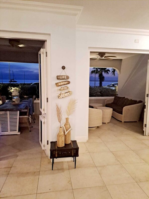 An open-plan living area with a view of the sea, a cozy seating area, and a wall-mounted sign with a life quote.
