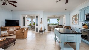 A spacious living room with a large TV, a dining area with a blue table, and a kitchen with blue cabinets. - Oceanfront large 4-p luxury groundfloor apartment  (Kralendijk)