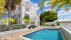 A pool area with a stone floor, palm trees, and a white building with balconies. - Oceanfront large 4-p luxury groundfloor apartment  (Kralendijk)