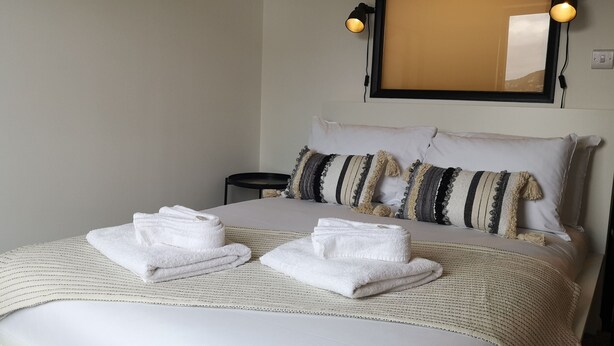 A neatly made bed with white linens and two folded towels, a bedside table, and two wall-mounted lamps. - Eastcliff Escape Folkestone (Folkestone)