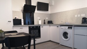 A modern kitchen with a built-in oven, microwave, and washing machine. There is a dining table with chairs and a small potted plant. - Eastcliff Escape Folkestone (Folkestone)