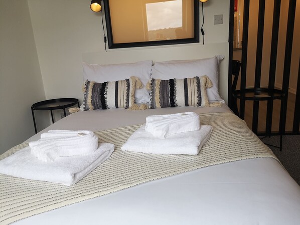 A neatly made bed with two pillows, a bedside table, and a chair.