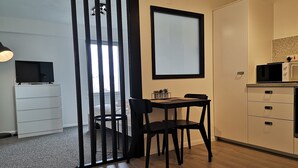 A modern kitchen with a dining area, a TV on a white cabinet, and a microwave on the countertop. - Eastcliff Escape Folkestone (Folkestone)