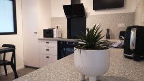 A modern kitchen with a microwave, toaster, kettle, and a flat-screen TV mounted on the wall. - Eastcliff Escape Folkestone (Folkestone)