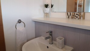 A bathroom with a white sink, a towel rack, a mirror, and a shelf with a plant and a 'WASH' sign. - Eastcliff Escape Folkestone (Folkestone)