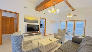 Een woonkamer met een televisie, bank, stoelen en een eethoek met een tafel en stoelen.