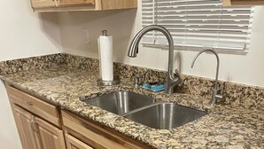 A kitchen with granite countertops, stainless steel sinks, wooden cabinets, and a dishwasher.
