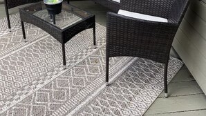 A patio area with wicker furniture, including two chairs and a table, and a patterned rug.
