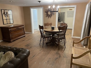 A dining area with a wooden table and chairs, a chandelier, and a wooden dresser.