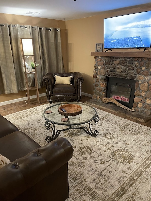 A living room with a stone fireplace, a leather sofa, a coffee table, and a television mounted above the fireplace.