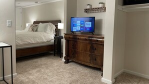 A bedroom with a bed, bedside table, dresser, and a television displaying streaming services.