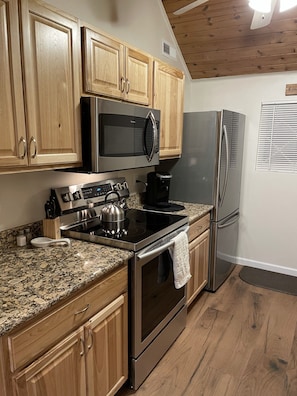 A kitchen with wooden cabinets, a stainless steel microwave, a refrigerator, a stove, and a coffee maker.